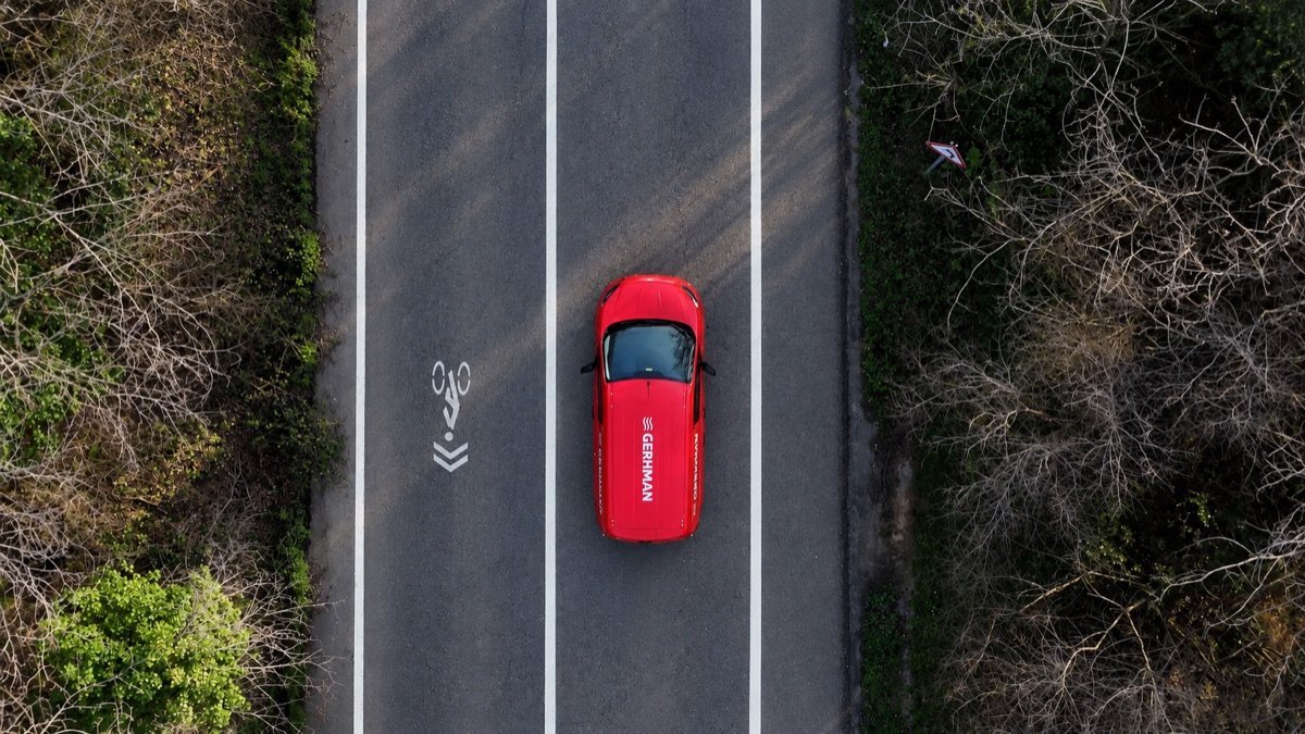Overhead view of a red Gerhman van on a tree-lined road.
