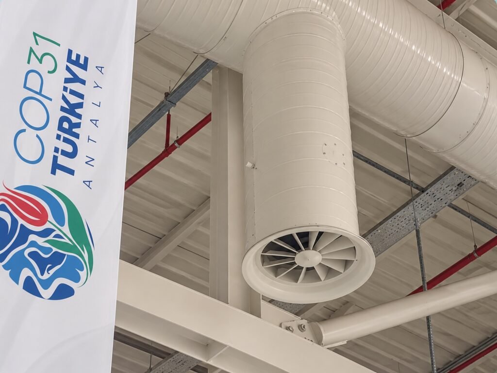 Close-up of a NOVA+ 400 diffuser connected to circular ductwork beside a COP31 banner